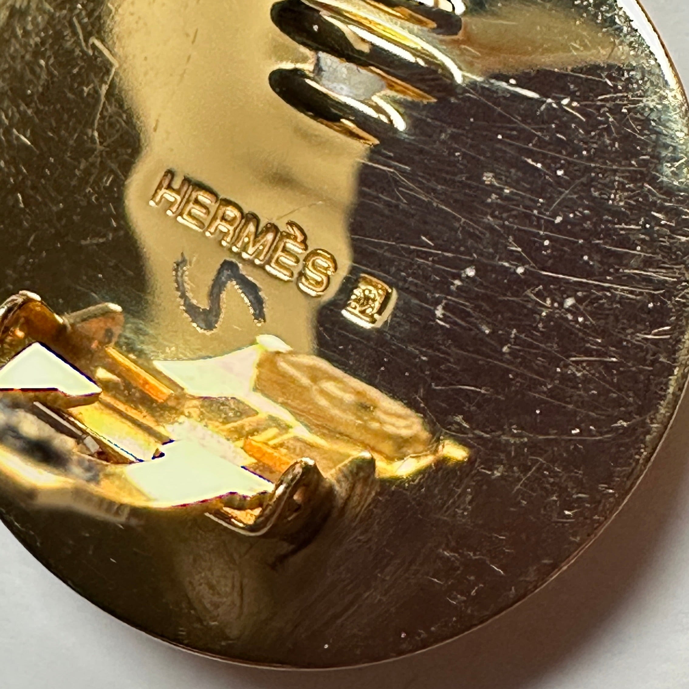 Macro sur la gravure "HERMÈS" et le marquage "S" (Ventes Privées) au dos du clip doré, attestant de l'authenticité.