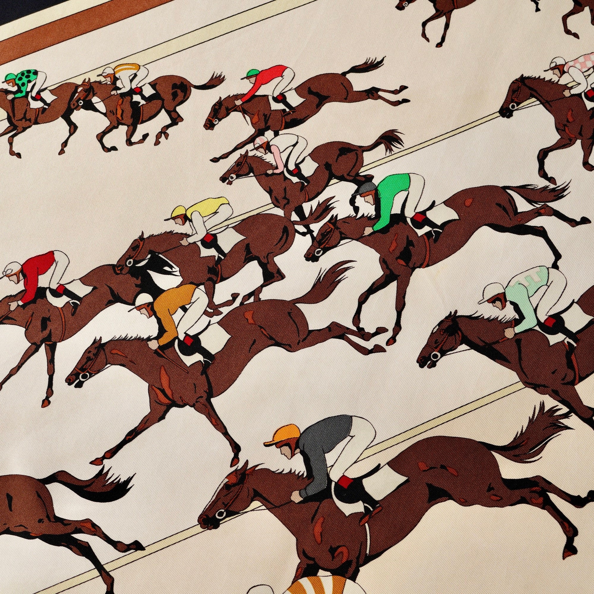 Détail du carré Hermès "Les Courses" : un jockey en casaque rouge et or franchissant une bande noire. Soie texturée.