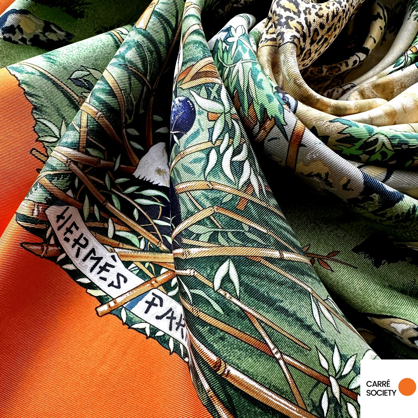 Vue rapprochée du foulard roulotté : texture soyeuse, bordure orange vif contrastant avec les tons verts.