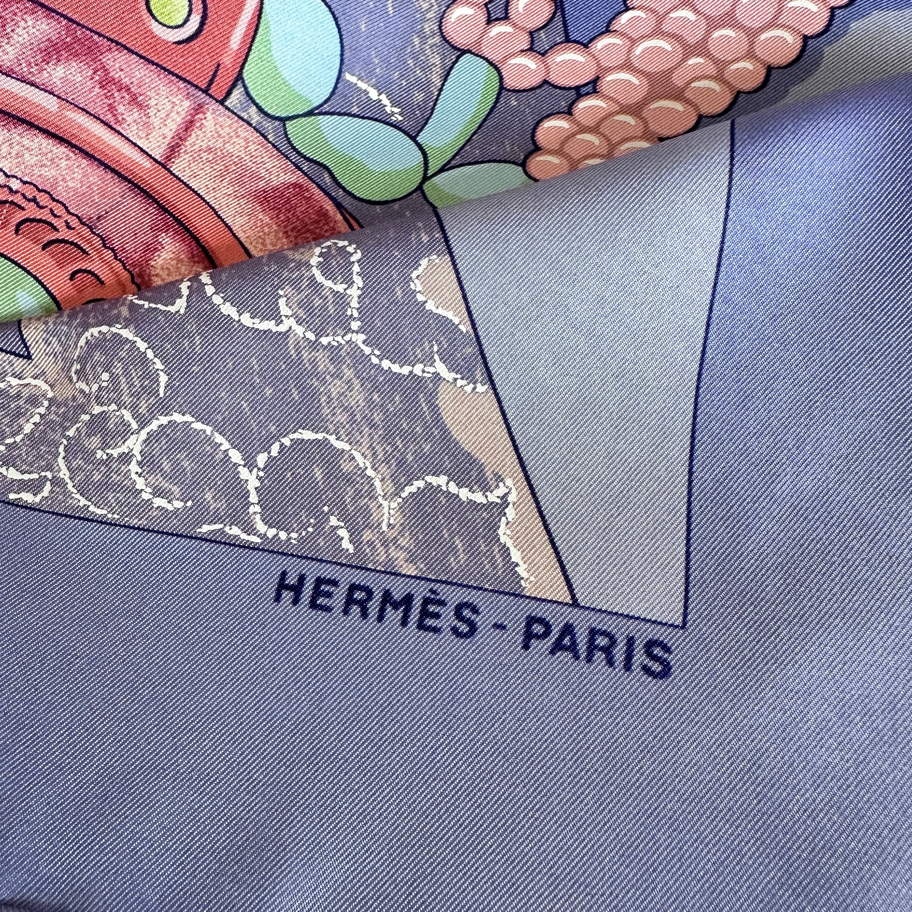 Signature Hermès Paris et détail du roulotté main sur fond bleu.